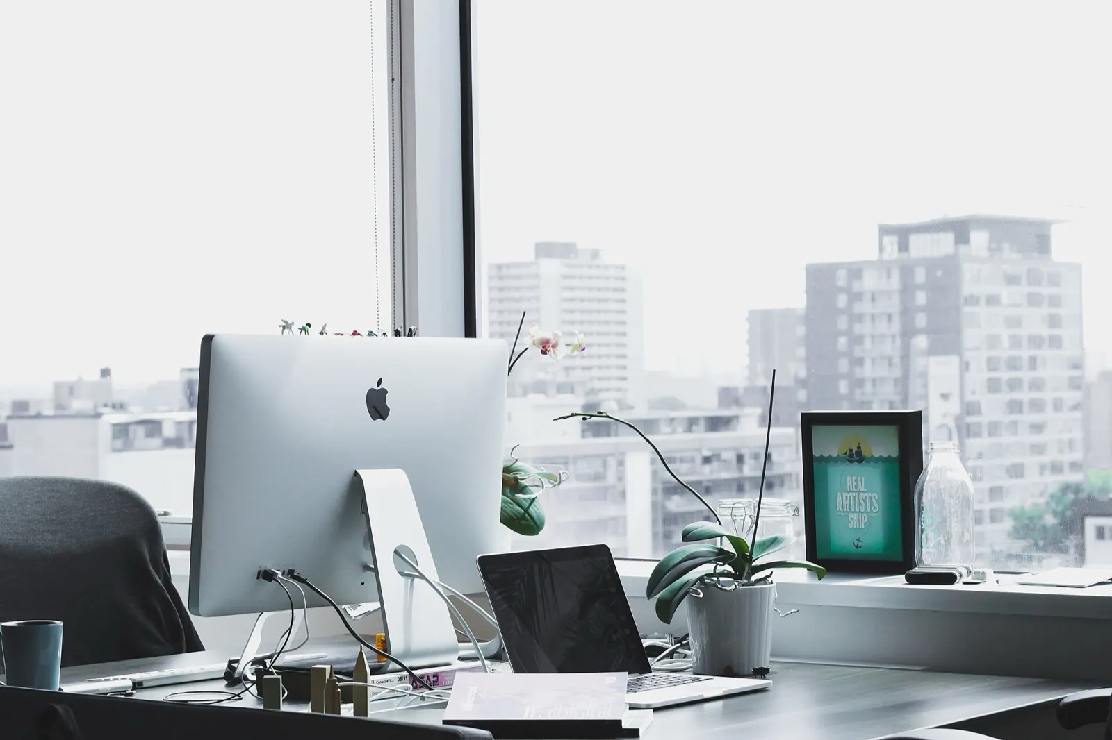 A tidy desk with a desktop computer beside a tall office window